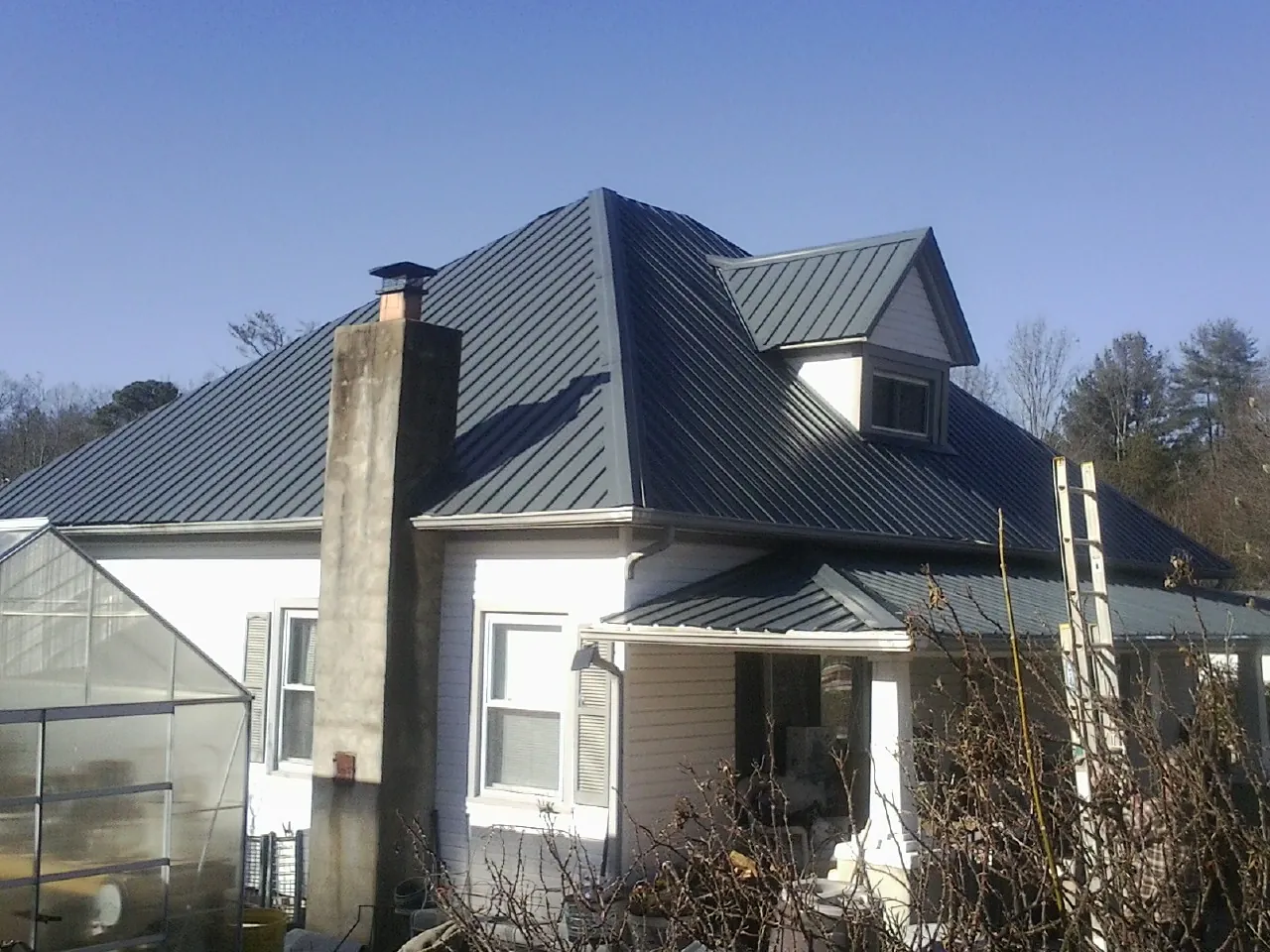 Dark blue standing seam metal roof on a white farmhouse with dormer — Slate & Tile Roof Repair by Roofing Brothers in Guernsey