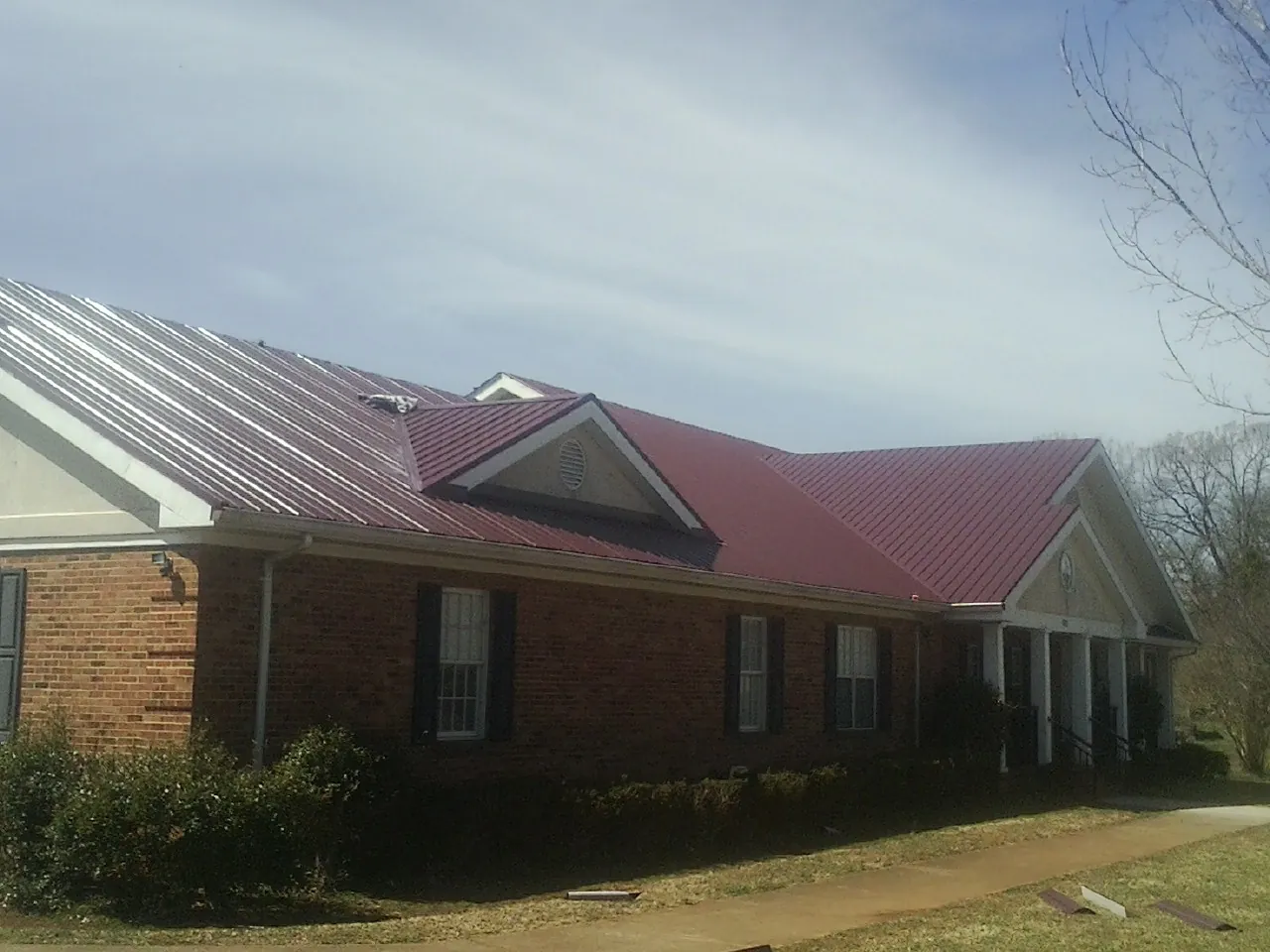 Red metal roof with gabled entries on a long brick building, from a Hail Damage Roof Repair job in Guernsey