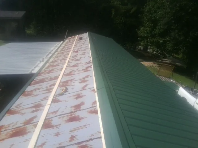 Old rusted panels beside newly installed green metal roofing — Wind Damage Roof Repair by Roofing Brothers in Guernsey