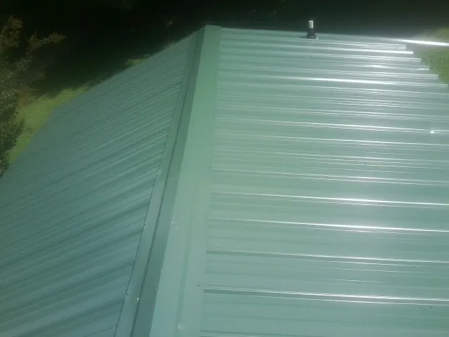 New green metal panels meeting at the ridge of a roof — Flat Roof Repair work by our crew in Guernsey