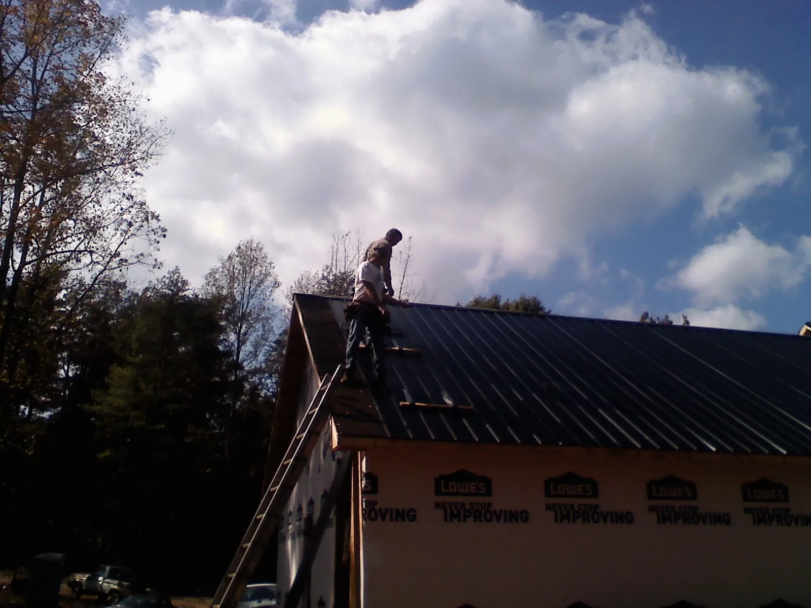 Roofer fastening dark metal panels high against a cloudy sky, from a Roof Inspection job in Guernsey