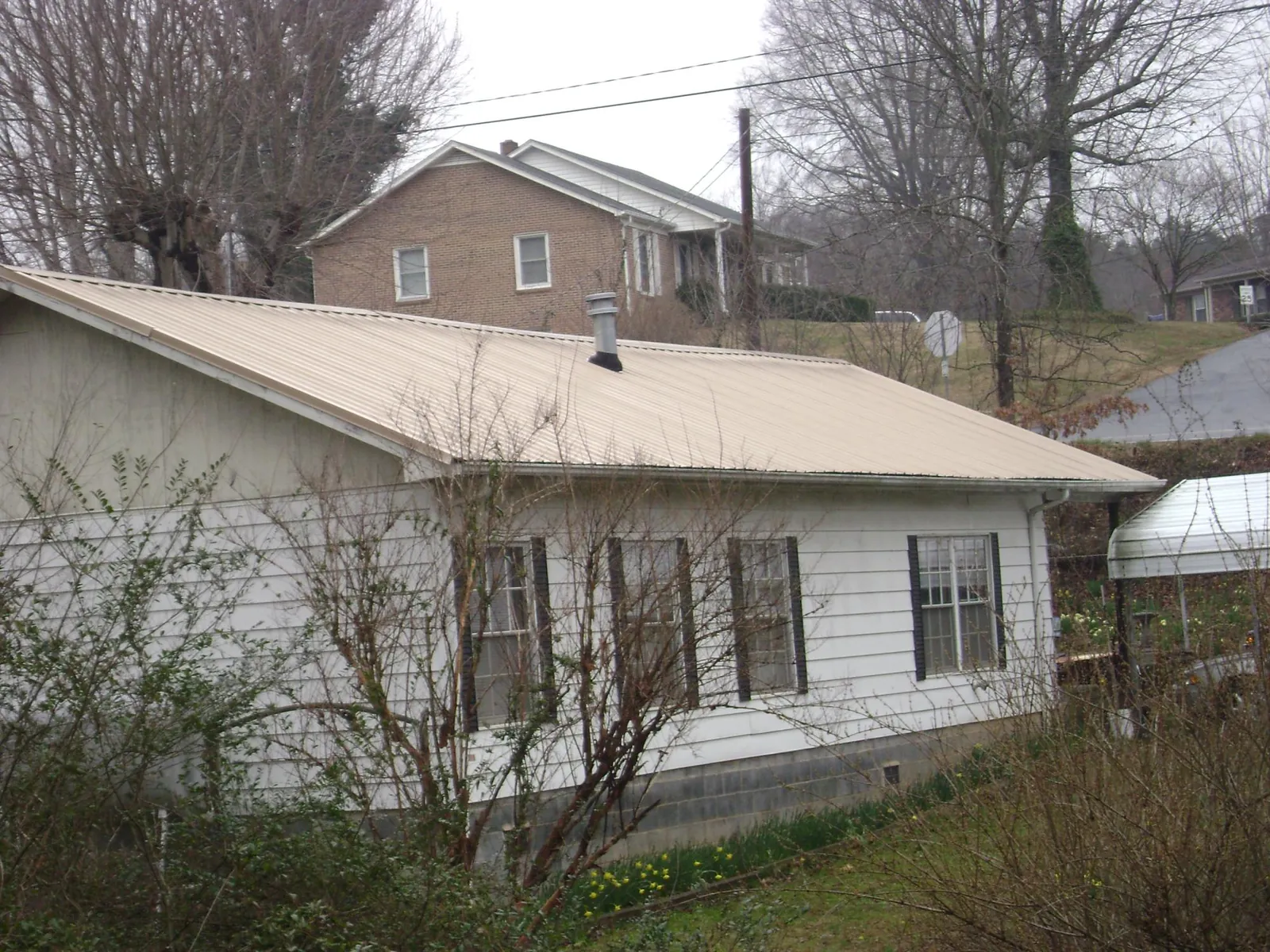 Tan metal roof on a white sided house set into a hillside — Commercial Roofing by Roofing Brothers in Guernsey
