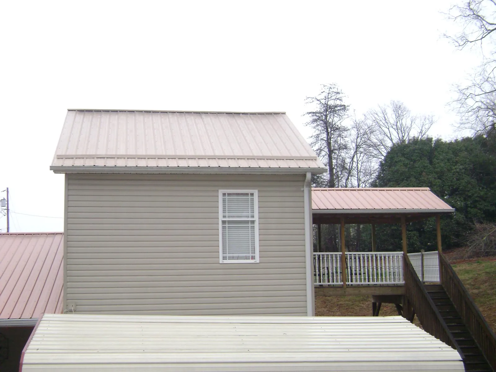 Tan metal roofs on a two story addition and attached porch, from a Roof Replacement job in Guernsey