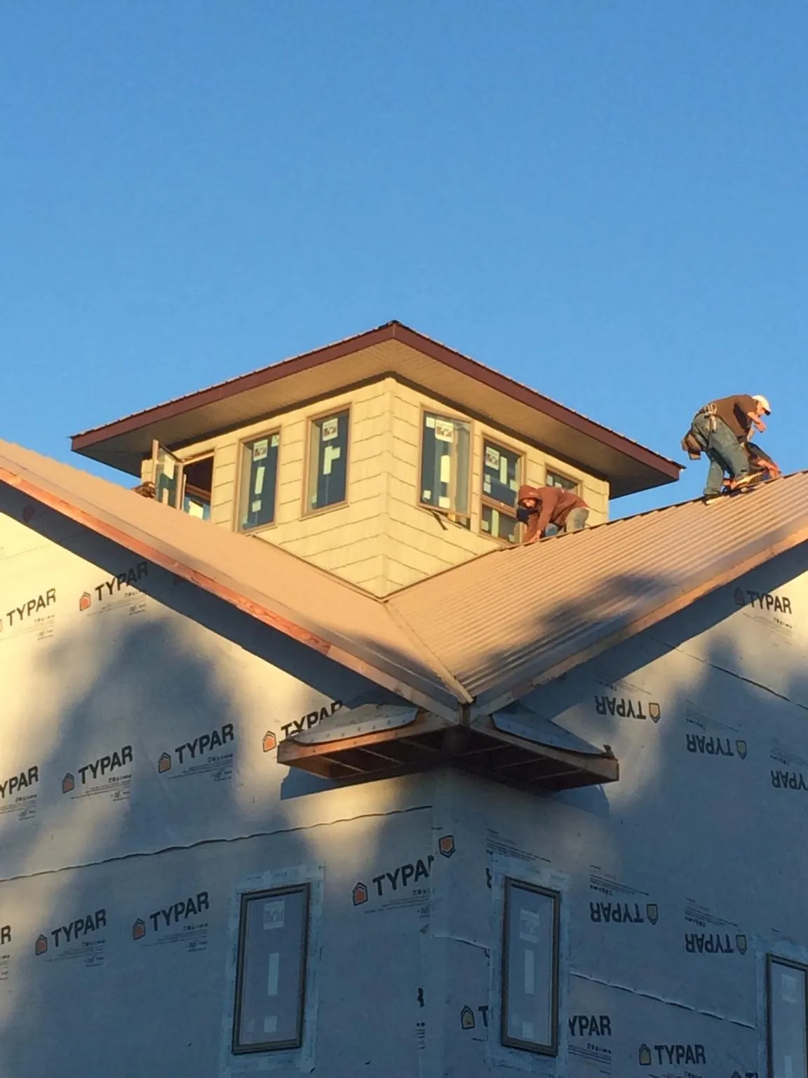 Roofers working around a rooftop cupola on a new metal roof at sunset — Roof Waterproofing in Guernsey by Roofing Brothers